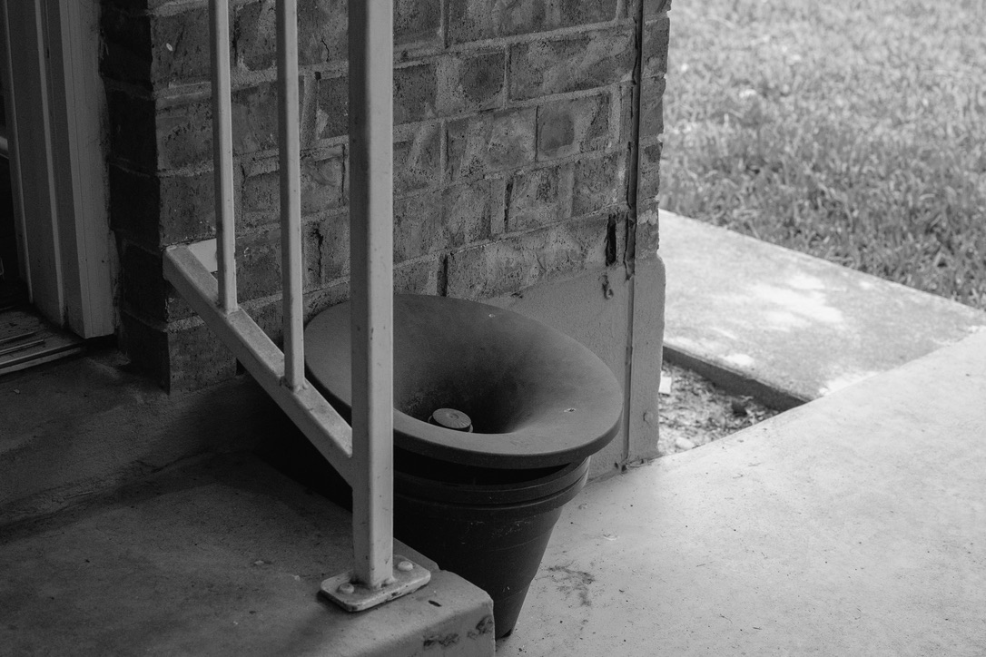 A weathered outdoor sink or basin mounted against a brick wall with metal support structure in black and white.